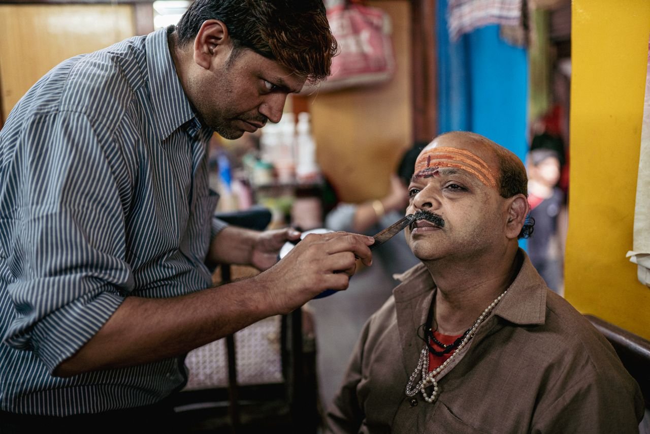 A barber performs a shave and face decoration at a traditional barbershop in Varanasi, India.