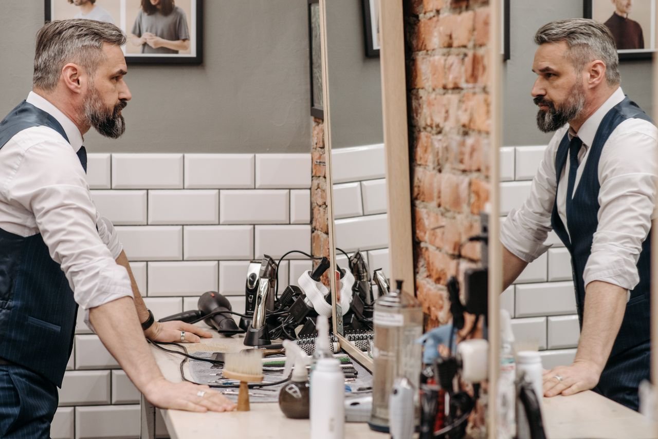 A bearded gentleman examines his reflection in a stylish barbershop setting.