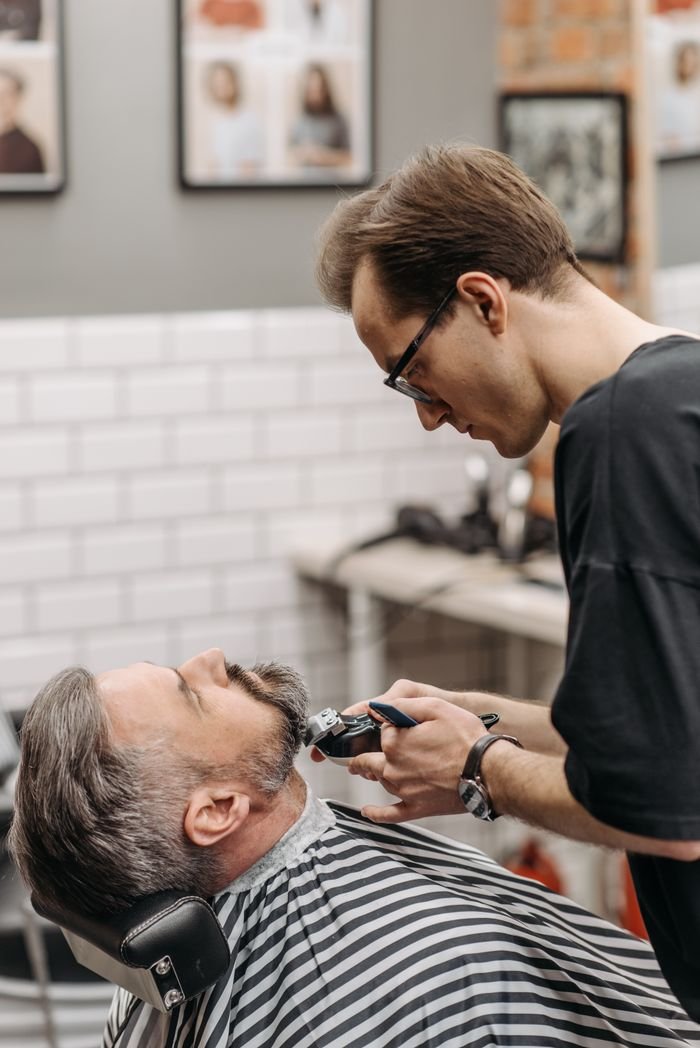 Barber using clippers to expertly trim beard of relaxed client in modern salon setting.
