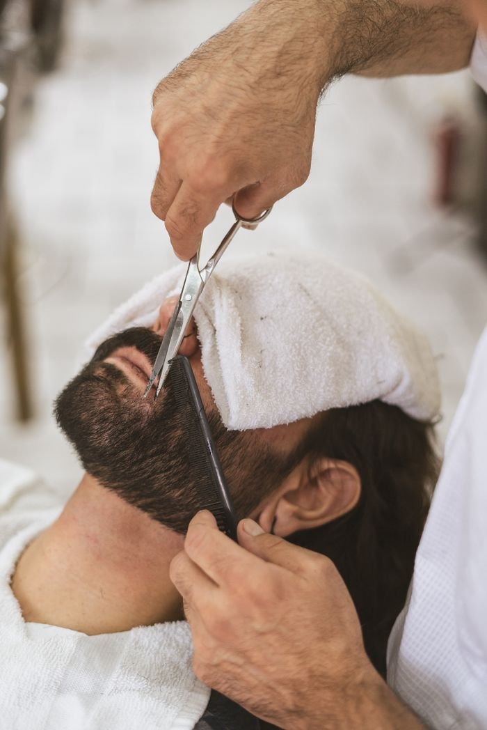 Close-up of a barber trimming a client's beard with scissors and comb.